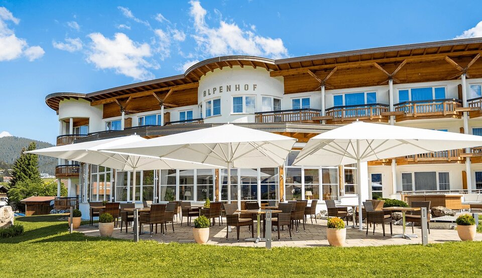 mehrere Sitzgruppen unter weißen Sonnenschirmen vor einem Hotel